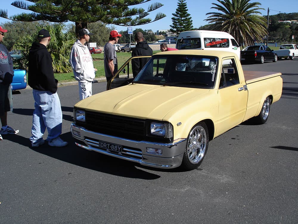 Pale yellow Datsun 1200 minitruck with custom canopy and chrome wheels at waterfront gathering at Half Way Havoc 2006 Nambucca Heads NSW - Minitruck Show Photos