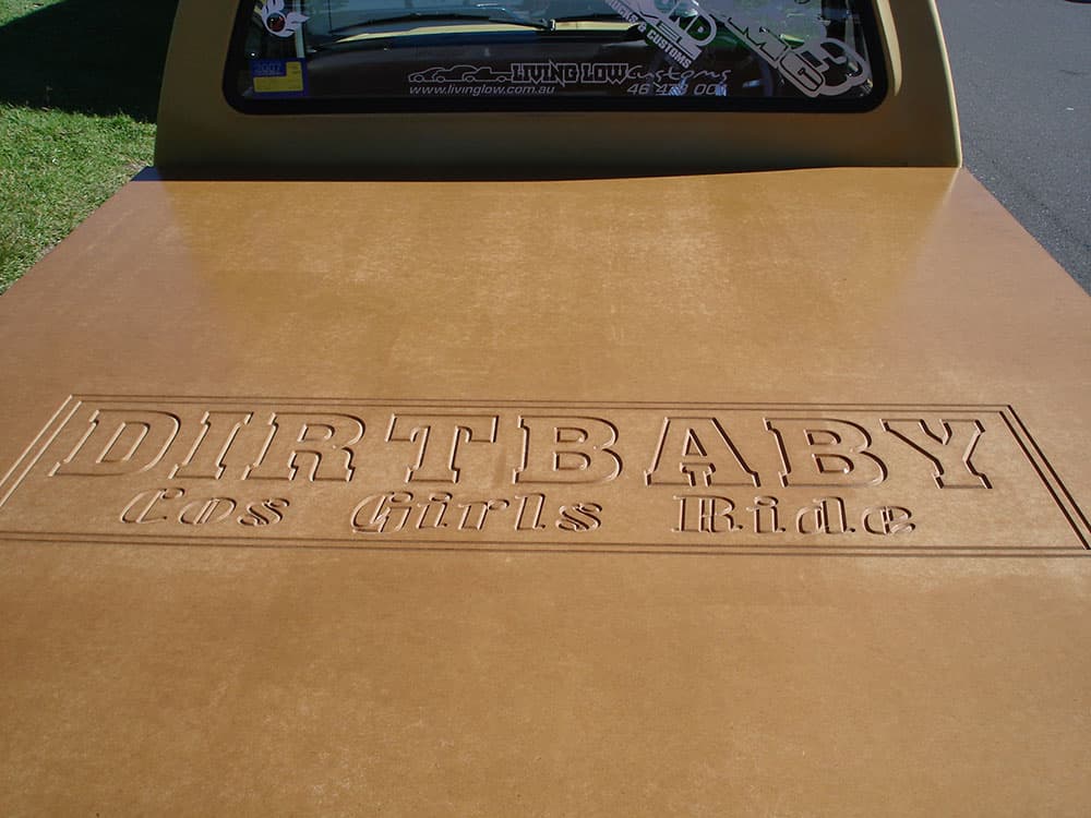 Custom painted tailgate detail showing DIRTBABY fans chicks ride embossed lettering on beige truck bed at Half Way Havoc 2006 Nambucca Heads NSW - Minitruck Show Photos