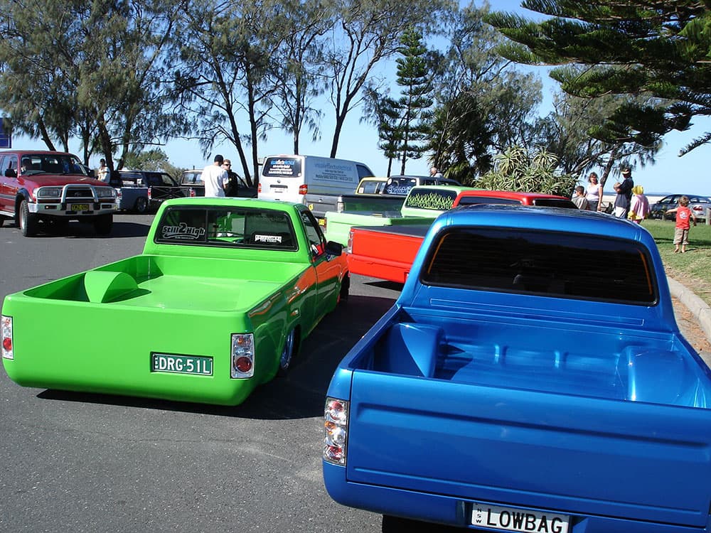 Bright green red and blue lowered minitrucks with LOWBAG plates lined up at waterfront Half Way Havoc