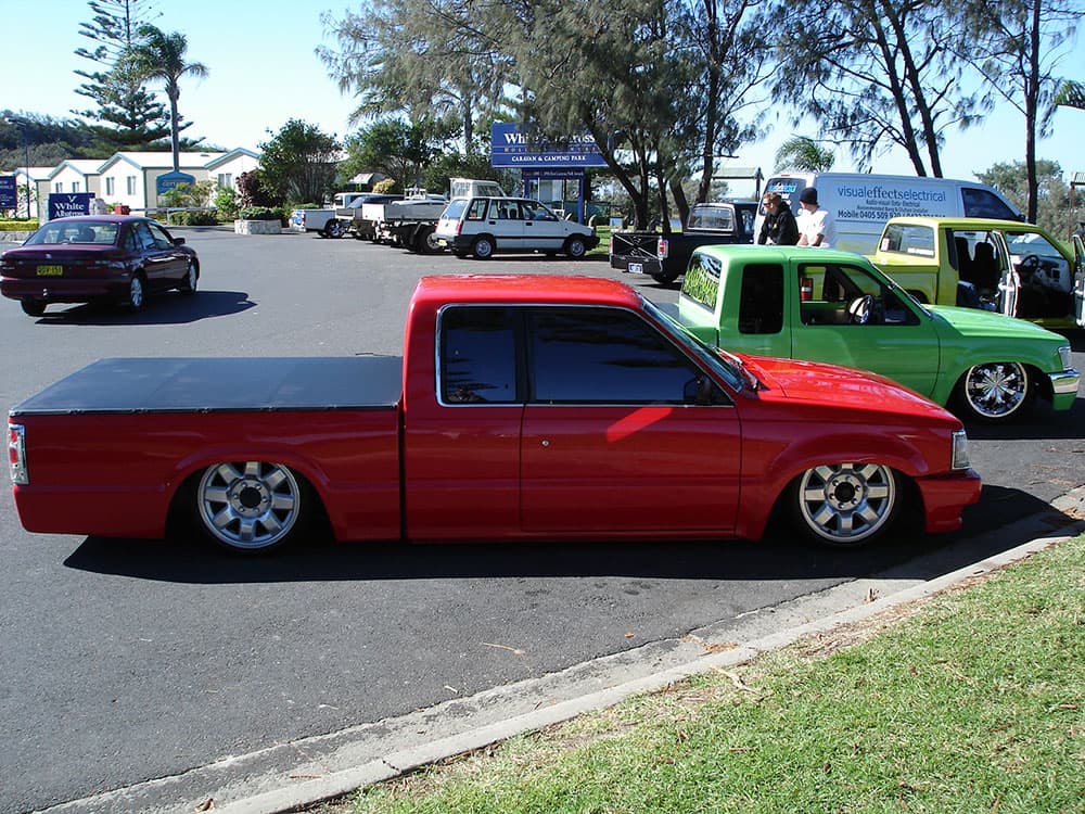 Bright red slammed Mazda B-series extended cab with custom wheels at Half Way Havoc waterfront event
