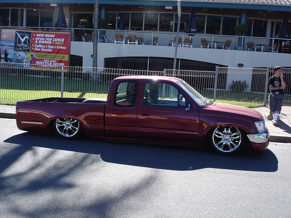 Burgundy metallic Toyota Hilux extended cab with chrome wheels parked at waterfront cafe Half Way Havoc