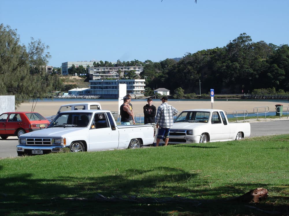 Two white slammed minitrucks with spectators gathered at waterfront park Half Way Havoc