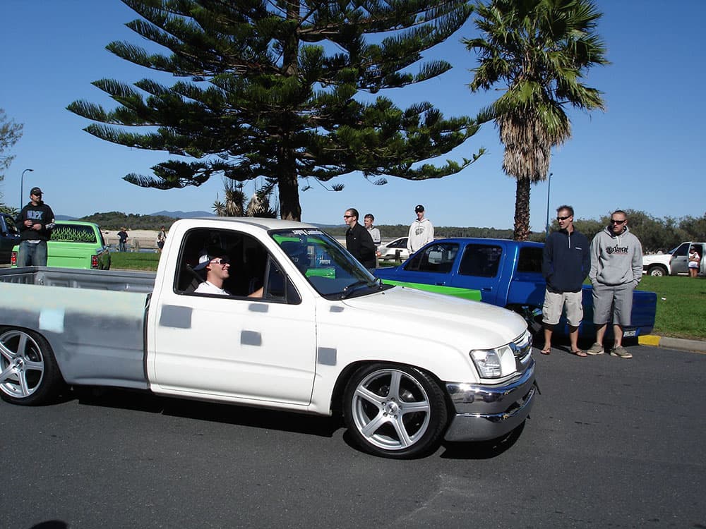 White lowered Toyota Hilux extended cab with spectators gathered around at Half Way Havoc waterfront