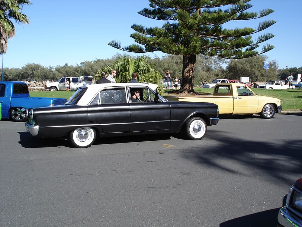Black classic Ford Falcon lowrider sedan with whitewall tires and chrome hubcaps at waterfront park at Half Way Havoc 2006 Nambucca Heads NSW - Minitruck Show Photos