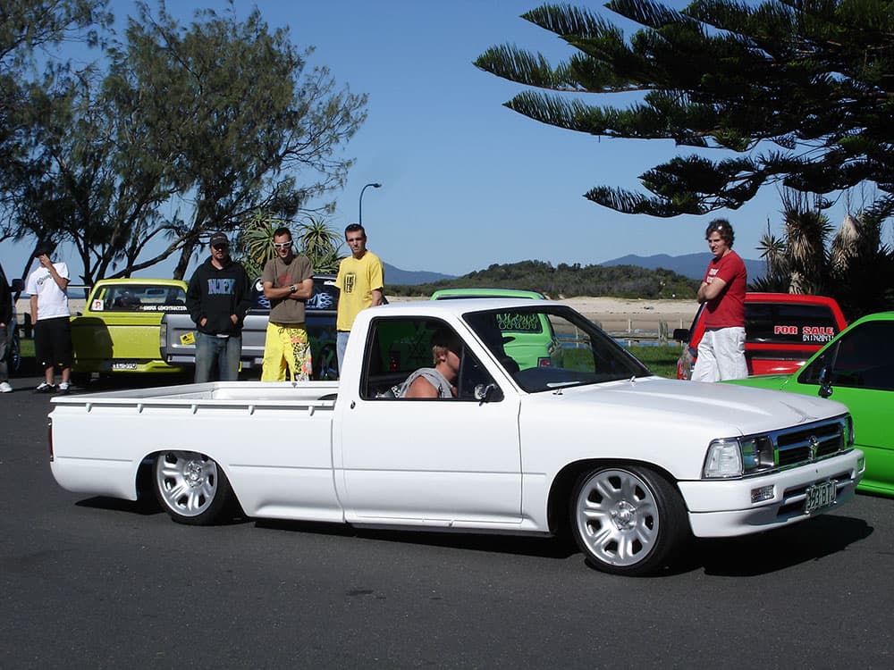 White lowered Toyota Hilux with chrome wheels and spectators at Half Way Havoc waterfront