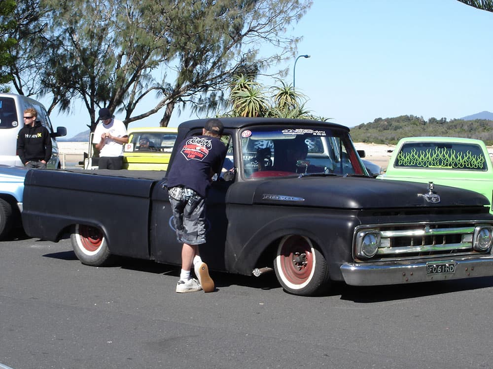 Matte black classic Chevrolet C10 pickup with red steel wheels and owner at Half Way Havoc