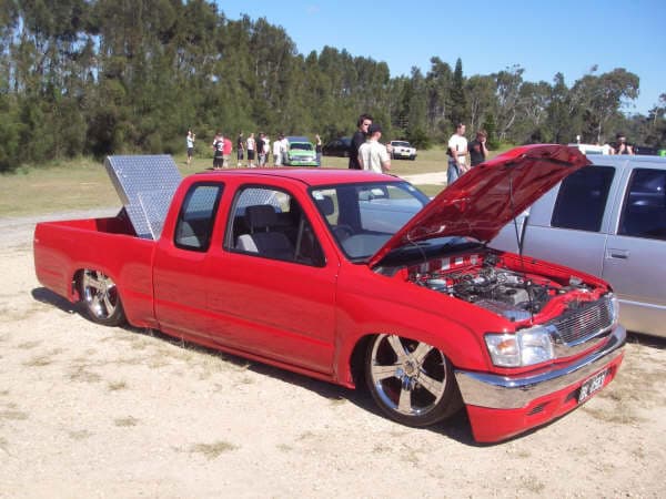 Bright red Toyota Hilux extended cab with hood open showing engine bay at grassy field gathering at Half Way Havoc 2006 Nambucca Heads NSW - Minitruck Show Photos