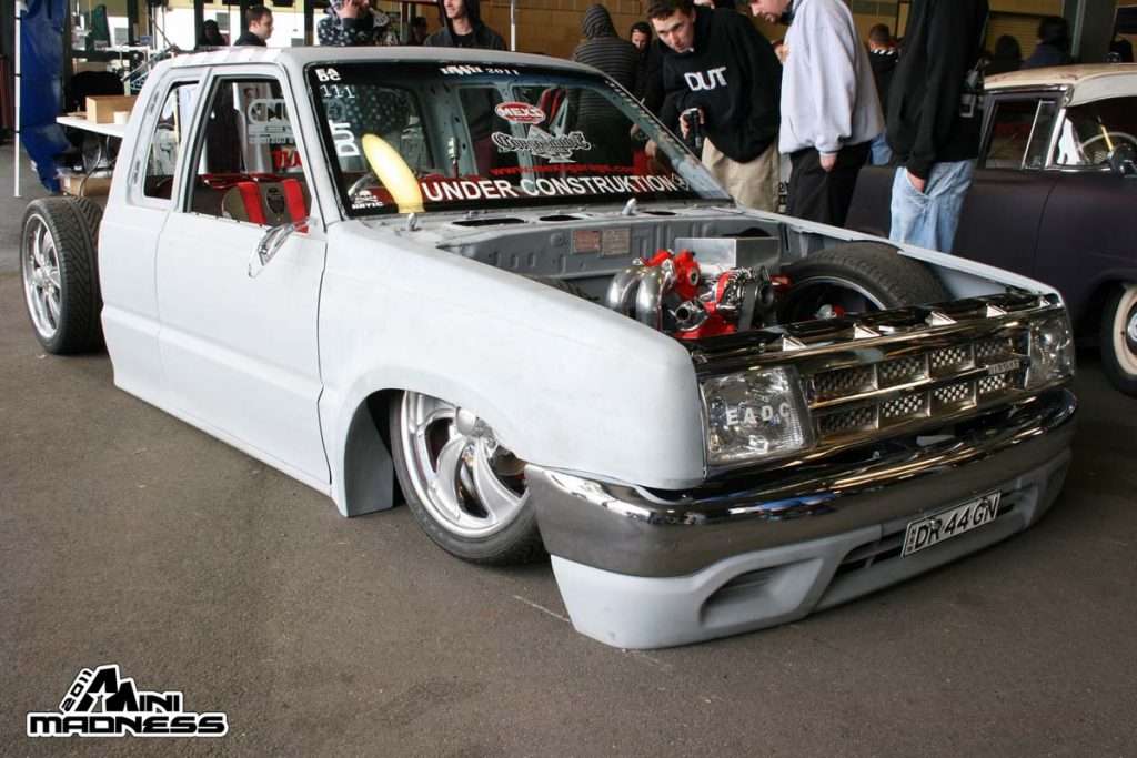 Minitruck in primer with UNDER CONSTRUCTION banner showing worked engine bay at indoor Mini Madness 2011