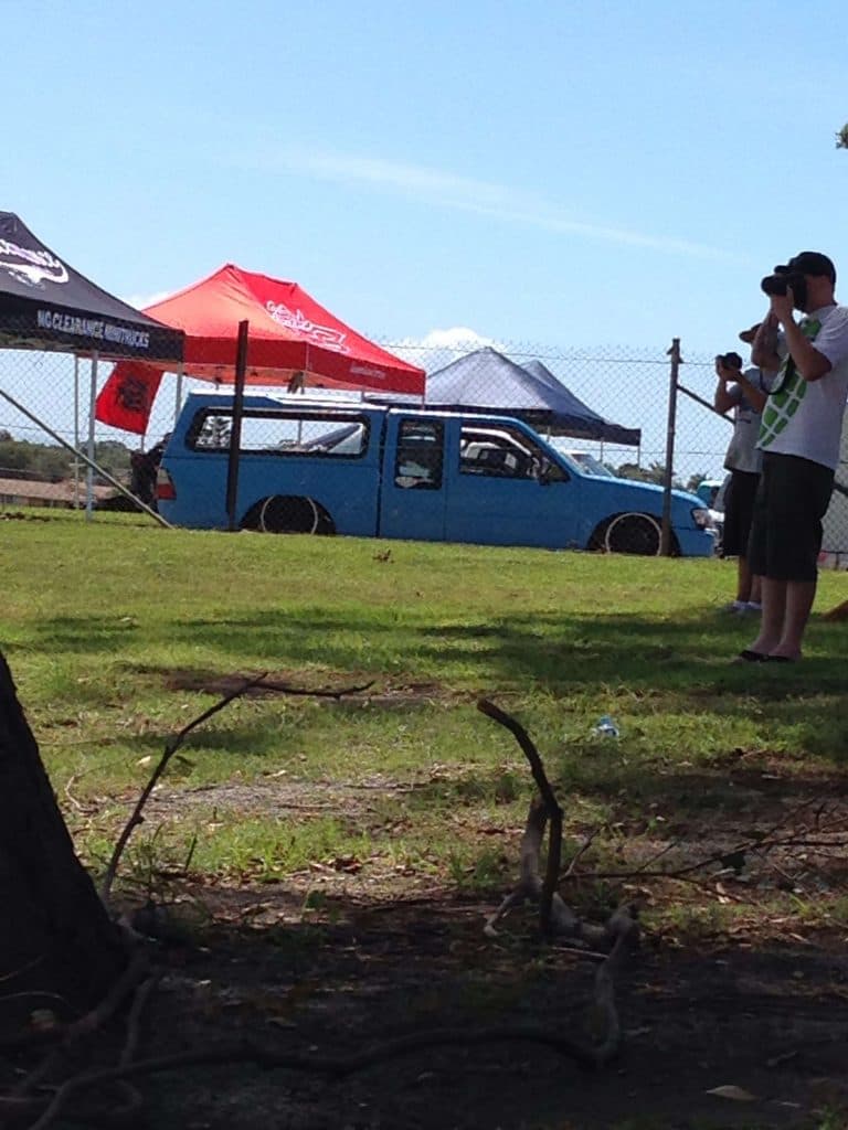 Blue slammed Holden Rodeo spacecab with extreme camber and vendor tents at Mini Madness 2014 Port Macquarie raceway